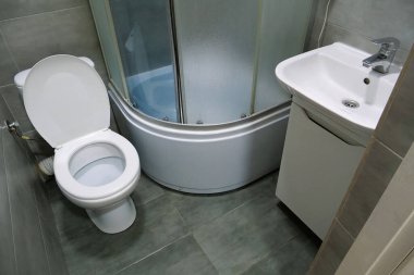 Toilet room interior with white toilet bowl, shower cabin and grey wall tiles
