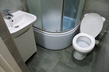 Toilet room interior with white toilet bowl, shower cabin and grey wall tiles