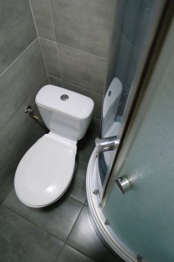 Toilet room interior with white toilet bowl, shower cabin and grey wall tiles