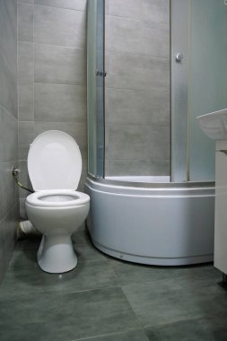 Toilet room interior with white toilet bowl, shower cabin and grey wall tiles