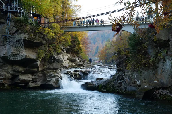 YAREMCHE, CARPATHIAN MOUNTAINS, UKRAINE, EKİM 16 Ekim 2022: insanlar Prut Nehri ve Probiy Şelalesi üzerindeki yaya köprüsünde. Ukrayna Karpatlarının en güzel ve güçlü şelalelerinden biridir.