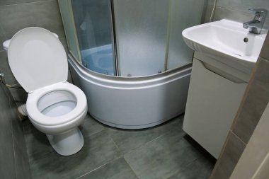 Toilet room interior with white toilet bowl, shower cabin and grey wall tiles