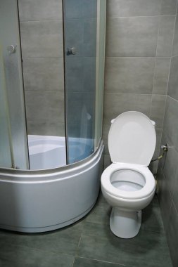 Toilet room interior with white toilet bowl, shower cabin and grey wall tiles