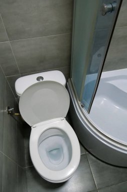Toilet room interior with white toilet bowl, shower cabin and grey wall tiles