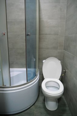 Toilet room interior with white toilet bowl, shower cabin and grey wall tiles