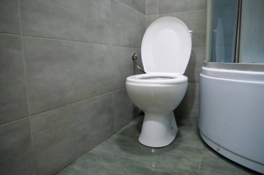 Toilet room interior with white toilet bowl, shower cabin and grey wall tiles