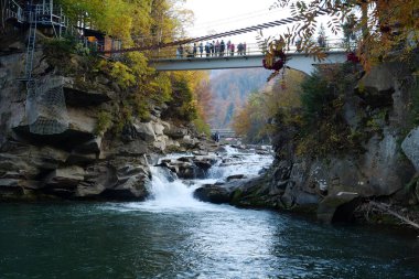 YAREMCHE, CARPATHIAN MOUNTAINS, UKRAINE, EKİM 16 Ekim 2022: insanlar Prut Nehri ve Probiy Şelalesi üzerindeki yaya köprüsünde. Ukrayna Karpatlarının en güzel ve güçlü şelalelerinden biridir.