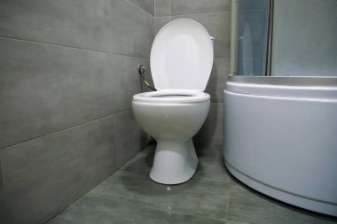 Toilet room interior with white toilet bowl, shower cabin and grey wall tiles