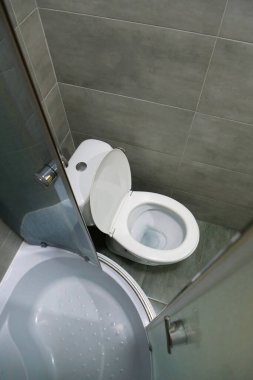 Toilet room interior with white toilet bowl, shower cabin and grey wall tiles
