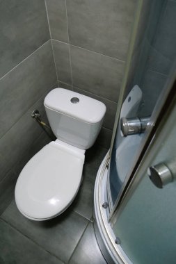 Toilet room interior with white toilet bowl, shower cabin and grey wall tiles