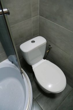 Toilet room interior with white toilet bowl, shower cabin and grey wall tiles