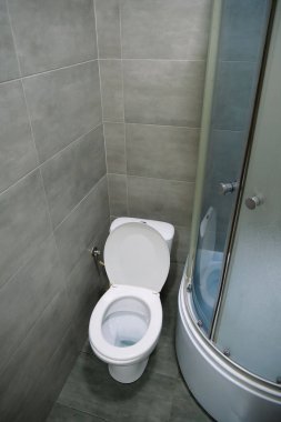 Toilet room interior with white toilet bowl, shower cabin and grey wall tiles