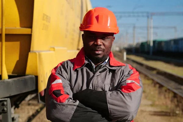 Yük treni terminalindeki Afrikalı Amerikalı demiryolu işçisi. Demiryolu işçisi üniformalı ve kırmızı şapkalı, kameraya bak.