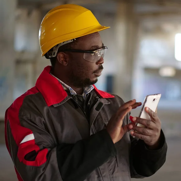 İnşaat alanında sarı şapkalı, akıllı telefonlu Afro-Amerikan işçiler var. İşçi el ele tutuşur akıllı telefon