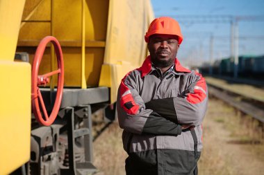 Yük treni terminalindeki Afrikalı Amerikalı demiryolu işçisi. Demiryolu işçisi üniformalı ve kırmızı şapkalı, kameraya bak.