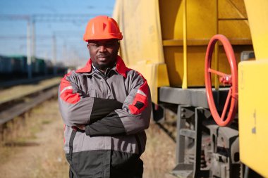 Yük treni terminalindeki Afrikalı Amerikalı demiryolu işçisi. Demiryolu işçisi üniformalı ve kırmızı şapkalı, kameraya bak.