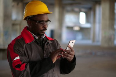 İnşaat alanında sarı şapkalı, akıllı telefonlu Afro-Amerikan işçiler var. İşçi el ele tutuşur akıllı telefon