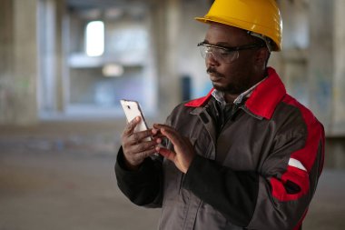 İnşaat alanında sarı şapkalı, akıllı telefonlu Afro-Amerikan işçiler var. İşçi el ele tutuşur akıllı telefon