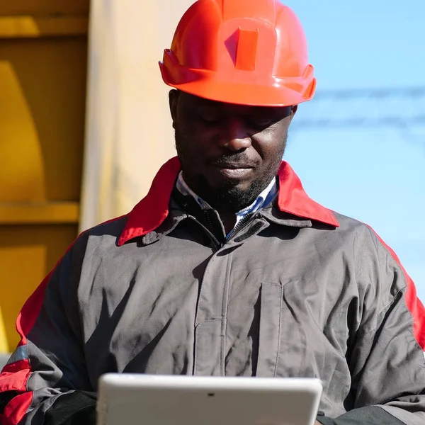 Yük treni terminalinde tablet bilgisayarı olan Afrika kökenli Amerikalı bir demiryolu işçisi. Üniformalı demiryolu işçisi ve bilgisayarlı kırmızı şapka. Demiryolu çalışanı el bilgisayarını tutuyor.