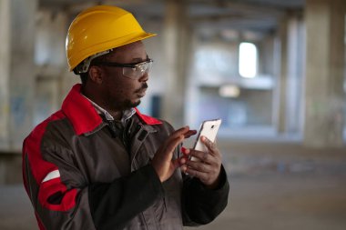 İnşaat alanında sarı şapkalı, akıllı telefonlu Afro-Amerikan işçiler var. İşçi el ele tutuşur akıllı telefon