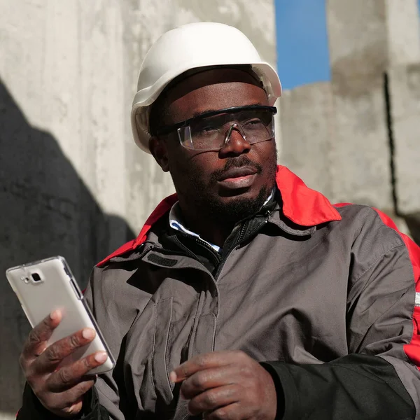 Siyah şapkalı ve koruyucu gözlüklü Afro-Amerikan işçiler inşaat alanında oturuyorlar. İşçi el ele tutuşup akıllı telefon ile etrafa bakıyor.