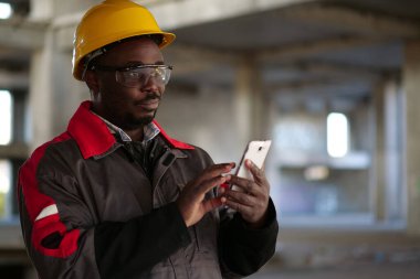 İnşaat alanında sarı şapkalı, akıllı telefonlu Afro-Amerikan işçiler var. İşçi el ele tutuşur akıllı telefon