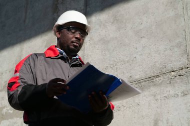 Afrikalı Amerikalı işçiler şantiyede duruyor ve çalışma evraklarına bakıyor.