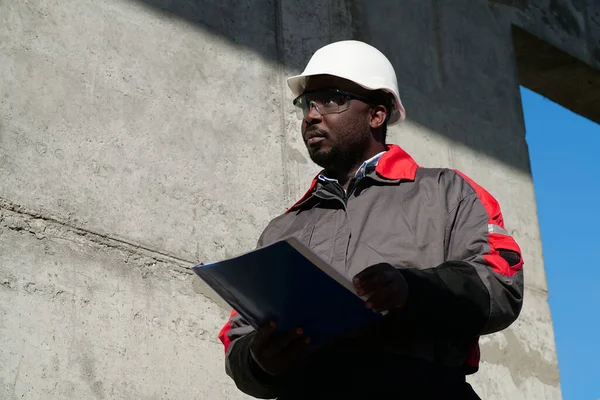 Afrikalı Amerikalı işçiler inşaat sahasında çalışma belgeleriyle duruyor ve ileriye bakıyor.