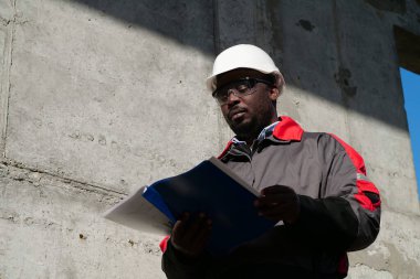 Afrikalı Amerikalı işçiler şantiyede duruyor ve çalışma evraklarına bakıyor.