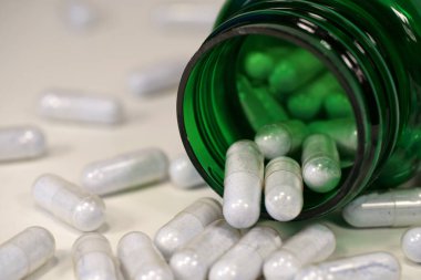 Capsules with blue powder and open green container lies on the white table. In reality these are tablets of copper in chelated form clipart