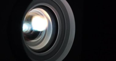 Projektör merceği yakın plan çalışıyor. Sinema salonu. Çalışan projektörlerin lensleri renk değiştirir. Film projektörle gösterilir. Farklı renklerin ışığı lenslerden geçer.