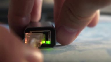 Adam bir internet kablosunu adaptör kullanarak bir dizüstü bilgisayara bağlıyor. Yeşil ve sarı LED ışıklı ethernet kablo adaptörü. İnternet kablosu bağlantısı. Bilgisayara bağlı bir adaptör üzerinden internet kablosu
