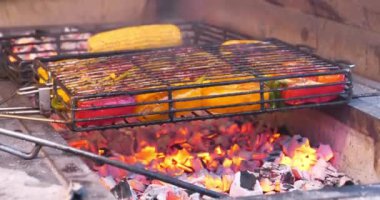 Biberler ızgarada sıcak kömürde pişirilir. Sarı ve kırmızı biberler barbeküde ızgara, kömür brazier. Alevler çıktı, aşçı biberleri sıcaktan temizledi.