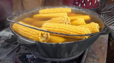 Kaynamış mısır, sıcak suyla birlikte büyük bir kazanda yatar. Ateş yakıyorum.