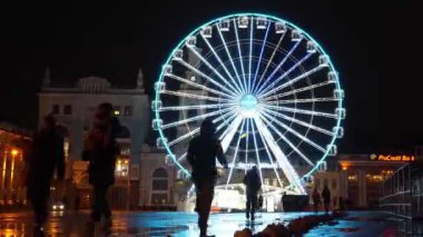 KYIV, UKRAINE, 25 ARALIK 2023: İnsanlar Ukrayna 'nın Kyiv kentinin tarihi Podil semtindeki Sözleşme Meydanı' nda akşam aydınlatmalarıyla dönme dolaba yakın yürüyorlar.