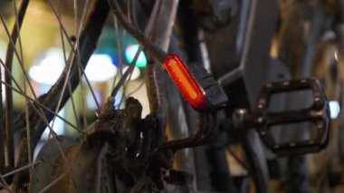 Bisikletin üstünde kırmızı lamba yanıp sönüyor, arabalı bir yolun yanında duruyor. Pizzacının önünde duran pizzacı bisikletli adam.