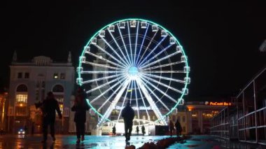 KYIV, UKRAINE, 25 Aralık 2023: İnsanlar Ukrayna 'nın tarihi Podil mahallesindeki Kyiv Meydanı' nda akşam aydınlatmalarıyla dönme dolaba yakın yürür. Zaman Uygulaması