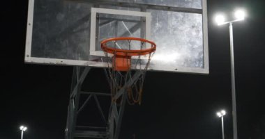 Basketbol sedyesi ve pota. Kırmızı basketbol çemberi. Spor sahası akşamları bir fenerle aydınlatılır. Sinema 4K 60fps video