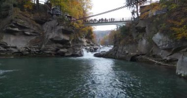 Ukrayna Karpatlarının en güzel ve güçlü şelalelerinden biri olan Prut Nehri ve Probiy Şelalesi üzerindeki yaya köprüsündeki insanlar. Sinema 4K 60 fps sesli video