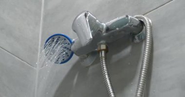 Banyoda duş başlığı, duvarlarda krom musluk ve gri fayanslar, kameraya doğru akan su.