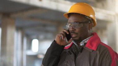 Afrikalı Amerikalı müteahhit akıllı telefondan konuşuyor. İnşaat alanındaki işletme müdürü cep telefonuyla konuşuyor