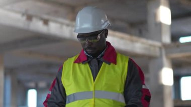 İnşaat alanındaki Afrikalı Amerikalı müteahhit tıbbi koruyucu maske taktı ve kollarını göğsüne bağladı.