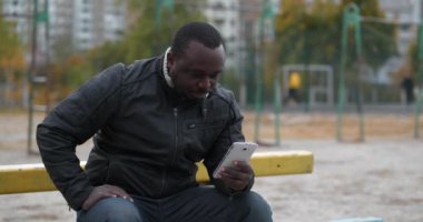 Yetişkin Afro-Amerikalı bir adam spor sahasında oturur ve video bağlantısıyla iletişim kurar.