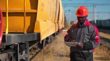 Yük treni istasyonundaki yük arabaları müfettişi Tablet PC 'ye not alır. Yük treni terminalinde tablet bilgisayarlı Afrikalı Amerikalı demiryolu işçisi.