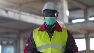 Tıbbi koruyucu yüz maskesi takan Afrikalı Amerikalı işçiler inşaat alanında durup kameralara bakıyorlar.