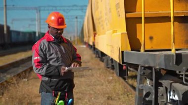 Yük treni istasyonundaki yük arabaları müfettişi tabletine notlar alır. Yük treni terminalinde tablet bilgisayarlı Afrikalı Amerikalı demiryolu işçisi.