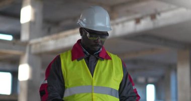 İnşaat alanındaki Afrikalı Amerikalı işçiler tıbbi koruyucu yüz maskesi takıp kollarını göğsüne bağlamış ve ileriye bakmış.