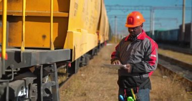Yük treni istasyonundaki yük arabaları müfettişi Tablet PC 'ye not alır. Yük treni terminalinde tablet bilgisayarı olan Afrikalı Amerikalı demiryolu işçisi.