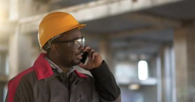 Afrikalı Amerikalı işçiler akıllı telefondan konuşur. İnşaat alanındaki işletme müdürü cep telefonuyla konuşuyor.
