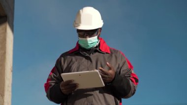 Slow Motion Afro-Amerikan işçi, inşaat alanında duruyor ve video bağlantısıyla tablet bilgisayarla konuşuyor.